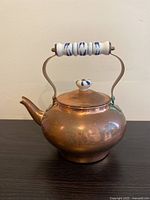 Front angle of the rounded copper plated teapot with porcelain blue and white decorative handle and lid knob.