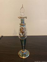 Front view of tall Egyptian hand blown glass bottle with decorative stopper, showing gold and blue striped design and clear glass stopper with flame-shaped top