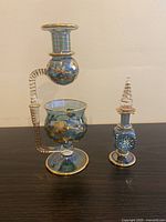 Photo of blue and gold hand blown glass oil burner and small matching bottle with stopper on black surface.