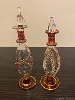 Two Egyptian hand blown glass bottles with stoppers, showing detailed decorative patterns and gold accents against a plain background.