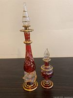 Photo of two Egyptian hand blown glass bottles with stoppers on a flat surface, showing their size and detailing