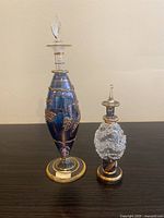 Photo showing two Egyptian hand blown glass bottles with stoppers, one tall blue with gold decoration and one smaller clear textured.
