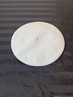 Top view of a grey wool beret showing the entire round shape and the distinctive central loop.
