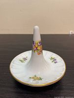 Front view of white porcelain ring holder with floral painting and gold edge trim.