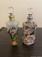 Front view of frosted glass bottle with floral enamel and rectangular silver-tone enamelled floral bottle