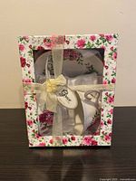 Floral tea cup and saucer set inside decorative floral box with a clear window and a golden ribbon tied.