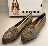 Front angled view of taupe leather Hush Puppies travel flats with snake print detail on pointed toe and Hush Puppies box behind