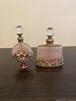 Front view of two decorative light rose colored glass bottles with jeweled brass floral designs and faceted stoppers