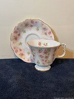 Cup shown on saucer with floral pattern and gold trim, side angle view