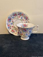 Side view of Royal Albert Mayfair cup and saucer on black cloth background showing floral pattern and scalloped edge of saucer