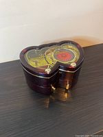Front angled view of the heart-shaped musical jewelry box showing the translucent top with gold and red musical mechanism and one drawer closed.