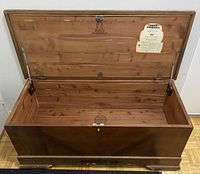 Front view of antique cedar chest with lid open showing internal cedar wood and brand labels, lock mechanism visible.