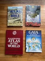 Four atlases displayed on a wooden floor: Atlas of the Bible, The Startup Touring Atlas of Britain, Illustrated Atlas of the World, Gaia: An Atlas of Planet Management