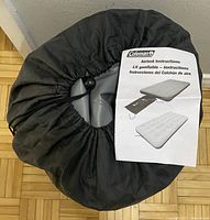 Rolled up Coleman All-Terrain queen airbed inside black drawstring carry bag, with airbed instruction sheet placed on top