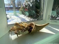 Cornucopia centrepiece displayed on a window sill with sunlight showing the woven horn and corn inside.