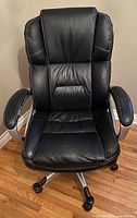 Front view of black cushioned faux leather office chair with padded armrests, retro stitching, and five caster wheels.