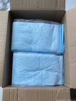 Open cardboard box showing stacked light blue folded disposable bed pads.