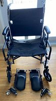 Front view of black wheelchair with cushioned arms and padded seat, foot and leg rests removed and placed in front of it.