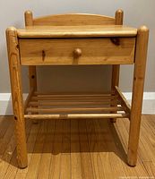 Front view of maplewood end table showing drawer and open spindle shelf below, placed on wooden floor against a wall.