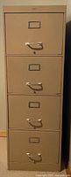 Front view of taupe metal filing cabinet showing four drawers, label holders, and handles.