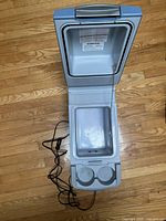 Top-down view of cooler opened showing interior compartment and cup holders with attached power cord on wooden floor.