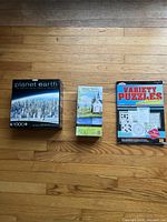 Three items laid out on wooden floor: BBC Planet Earth 1000-piece puzzle, 500-piece church puzzle, Variety Puzzles book.