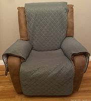 Front-facing view of a brown recliner with the sage green quilted cover on the backrest, seat, and armrests.