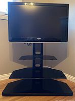 Front view of Samsung 35-inch LCD TV mounted on a black adjustable stand with three black glass shelves.