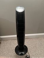 Full front view of black tower fan with vertical grills and solid round base