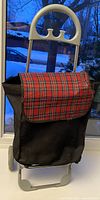 Front view of black shopping trolley with tartan flap and handle