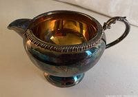 Copper plated creamer showing the side with handle and decorative rim detail.