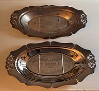 Two copper plated oval serving trays side by side, one with engraving and one without, showing the full top side of trays and decorative handles.