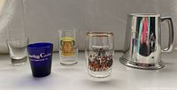 Set of four shot glasses and one pewter stein arranged in a row, showing all details on the glassware and stein