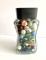 Full view of filled glass coffee jar showing variety of colorful vintage marbles inside.