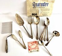 Full set of 12 silverplate serving pieces arranged with original guarantee and instruction pamphlet visible.