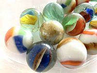 Close-up photo showing diverse glass marbles with colorful internal swirls including blue, orange, green, yellow, and white.