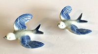 Pair of blue and white ceramic birds on a white background, showing front and top views of both pieces.