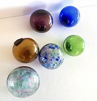 Six blown glass balls arranged on a white background showing variety of colors and styles.