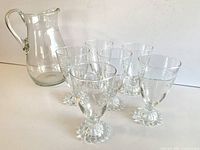 View of set showing six etched grape cluster glasses with beaded pedestal bases and clear glass pitcher with swallows and waves etching.