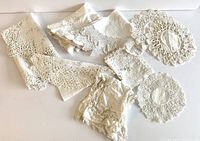 Nine various white or off-white vintage table linens showcasing lace, embroidery, and tatting work, laid out folded and stacked for a group view.