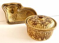 Two pottery kitchenware items side by side: a circular covered casserole and a lamb-shaped food mold.
