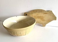 Photo showing the yellow ware batter bowl and pig shaped wooden cutting board side by side on a white surface