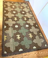 Full view of the rectangular hooked rug with geometric floral pattern in earth tone colors on hardwood floor.