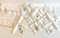 Overview of all 8 vintage white handkerchiefs displayed, showing varied embroidered floral motifs and fabric edges.
