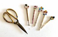 Full view of 5 lace bobbins and a pair of metal scissors with rattan handles, all arranged on a white background.