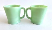 Two vintage Fire-King jadeite mugs shown side by side from front, displaying color, shape, and handles.