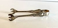 Side view of sterling silver sugar tongs showing clasp detail and ornate pattern on handle