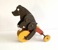 Side view of the vintage wooden bear toy, showing black painted body with jointed limbs and yellow wheels.
