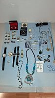 Full overview of all jewelry and watches laid out on a flat surface including cufflinks, watches, necklaces, pendants, earrings, rings, tie clips, and money clip.