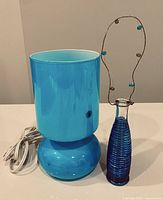 Photo of blue glass table lamp and elongated decorative blue glass vase together.